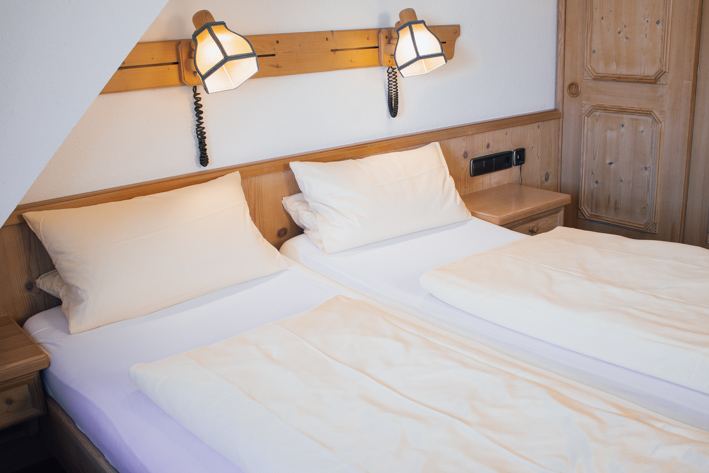 Gemütliches Doppelbettzimmer mit weißer Bettwäsche. Das Bett, die Nachttische sowie die Kleiderschränke sind aus schönem Holz.